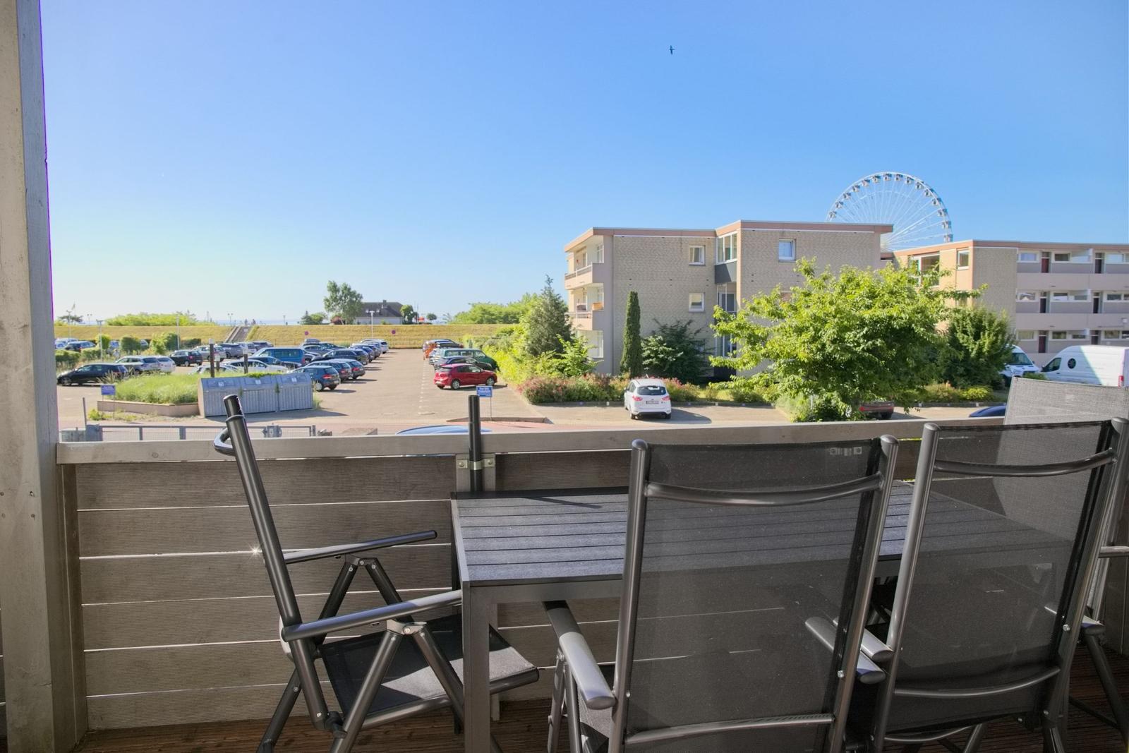 Terrasse mit Tisch und Stühlen. Blick auf Parkplatz und Gebäude mit Riesenrad.