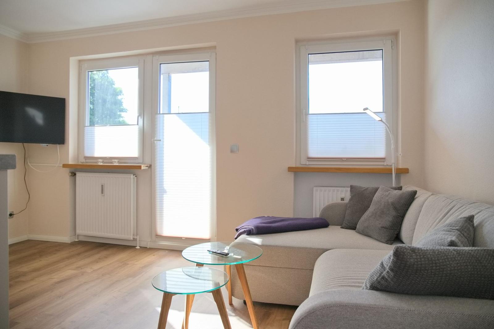 Wohnzimmer mit Sofa, zwei Glas-Tischen und Fenstern mit Jalousien.