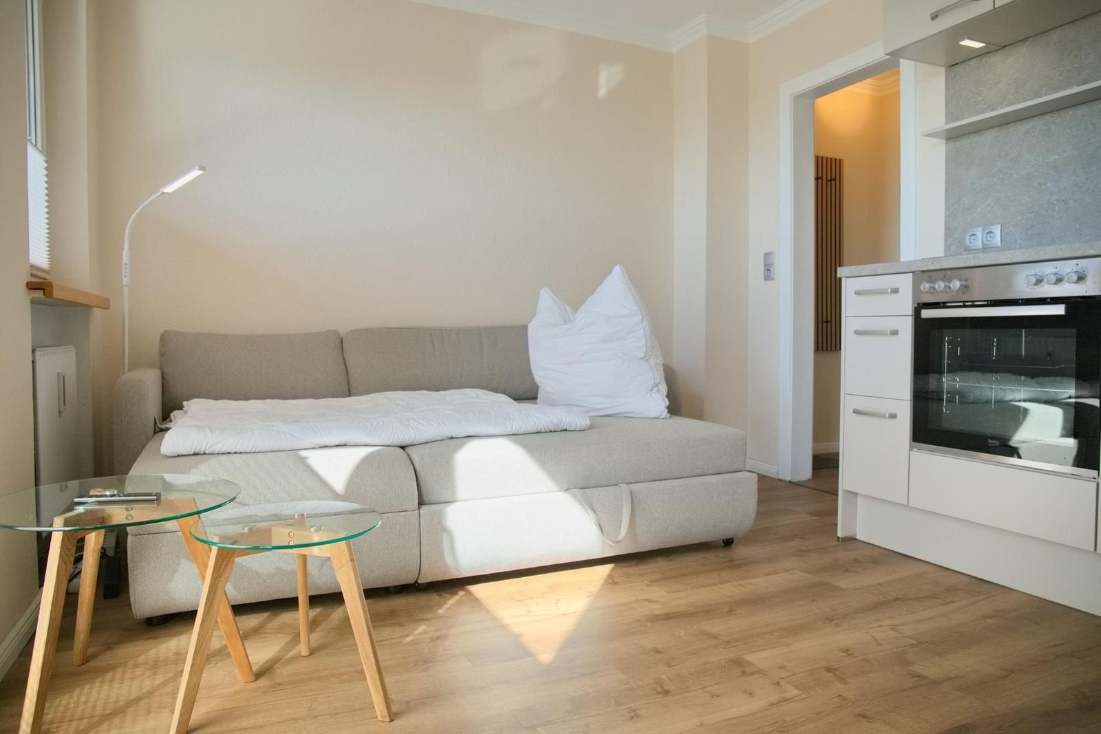 Wohnbereich mit Sofa, zwei Tischen und Küchenzeile.
