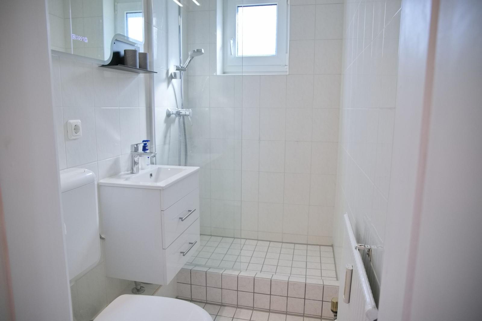 Badezimmer mit Dusche, Waschbecken und Toilette. Weiße Fliesen und Spiegelschrank.