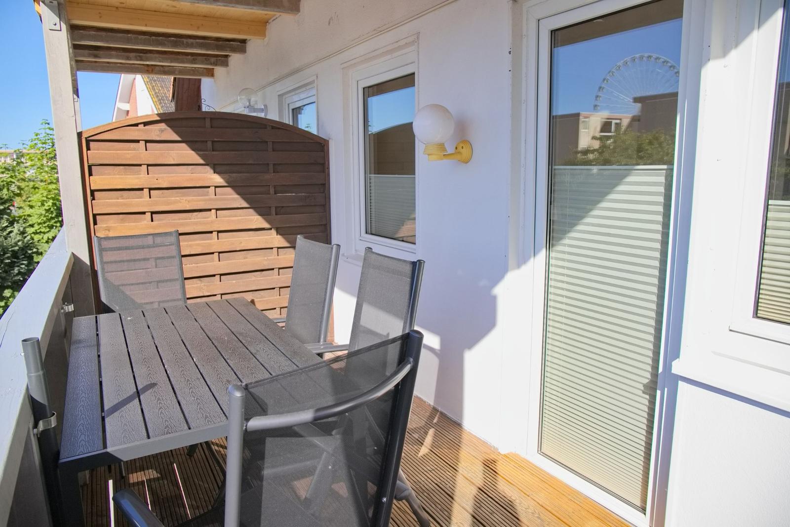 Terrasse mit Tisch und Stühlen, Holzgeländer und Fenster mit Jalousie.