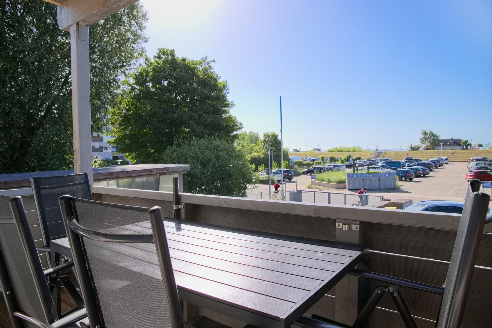 Terrasse mit Tisch und Stühlen. Blick auf Parkplatz und Bäume unter blauem Himmel.