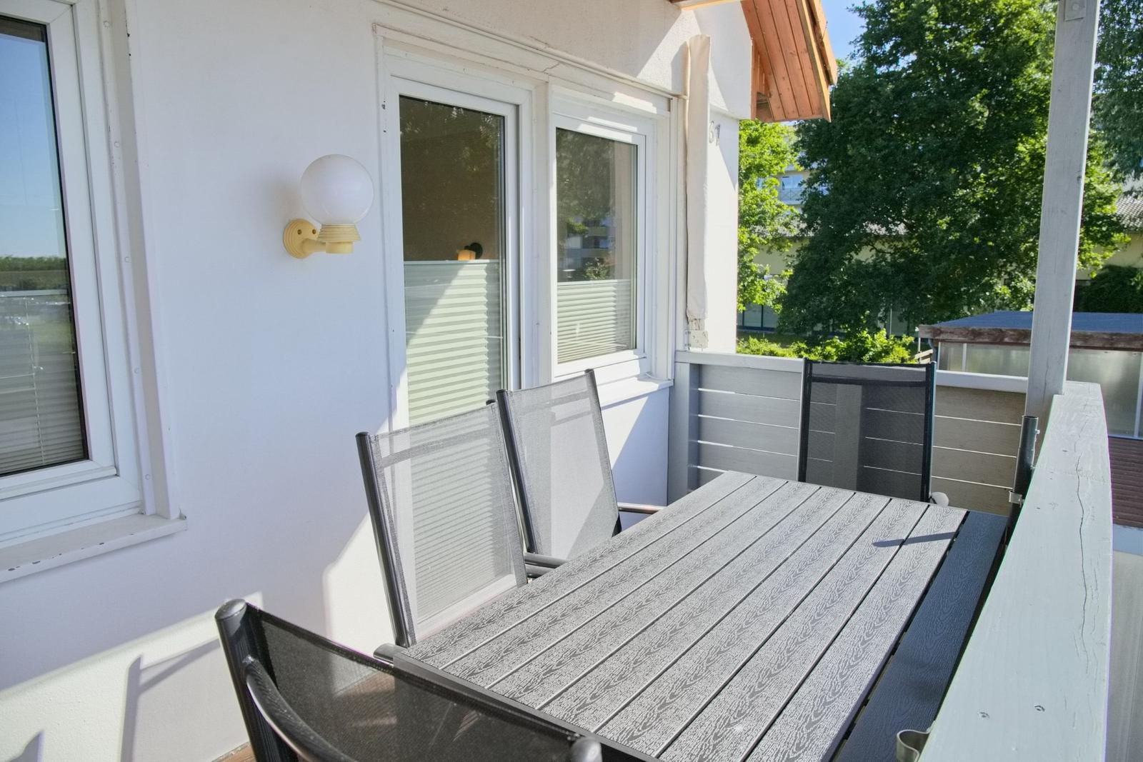 Terrasse mit Tisch und Stühlen, weiße Wand und Fenster, Außenbeleuchtung.