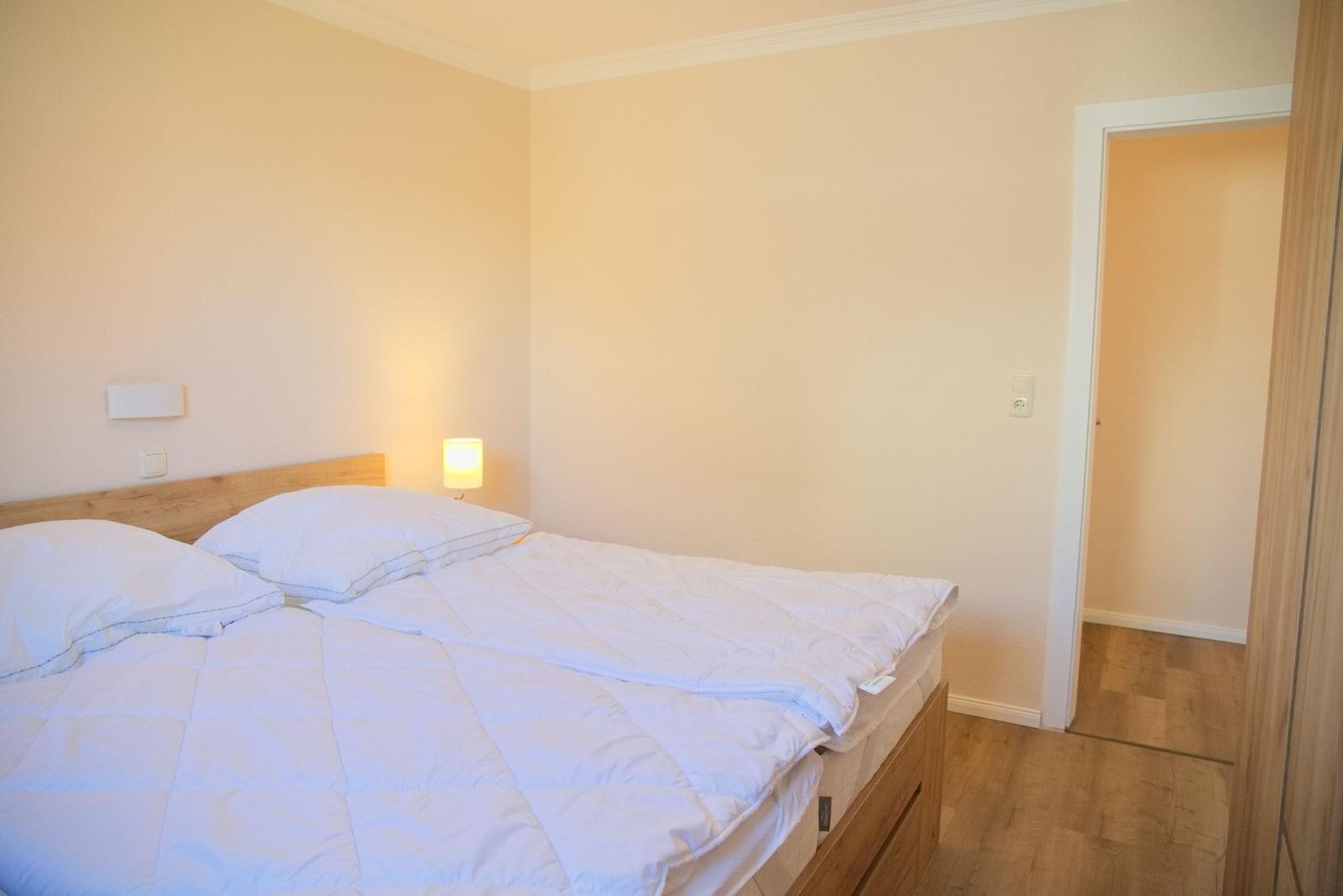Schlafzimmer mit Doppelbett, Nachttischlampe und Holzboden.