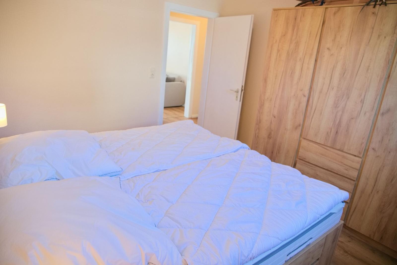 Schlafzimmer mit Bett, Kleiderschrank und Tür zum Wohnbereich.