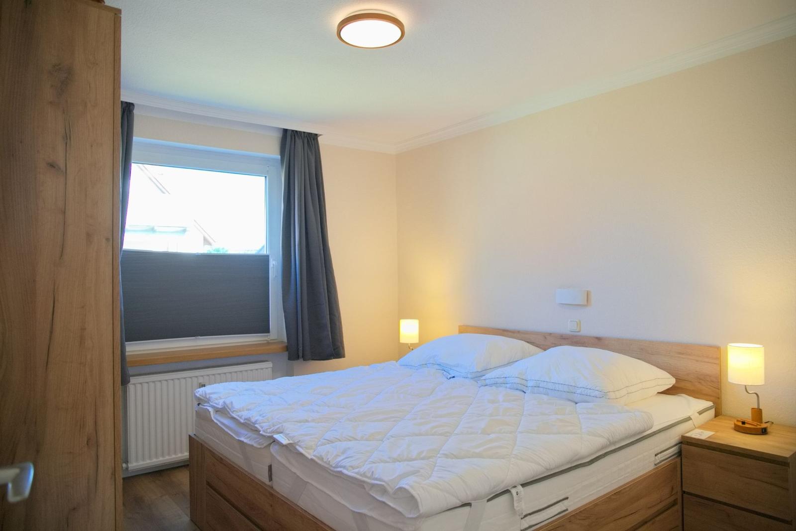 Schlafzimmer mit Doppelbett, Nachttisch und Fenster mit Vorhängen.