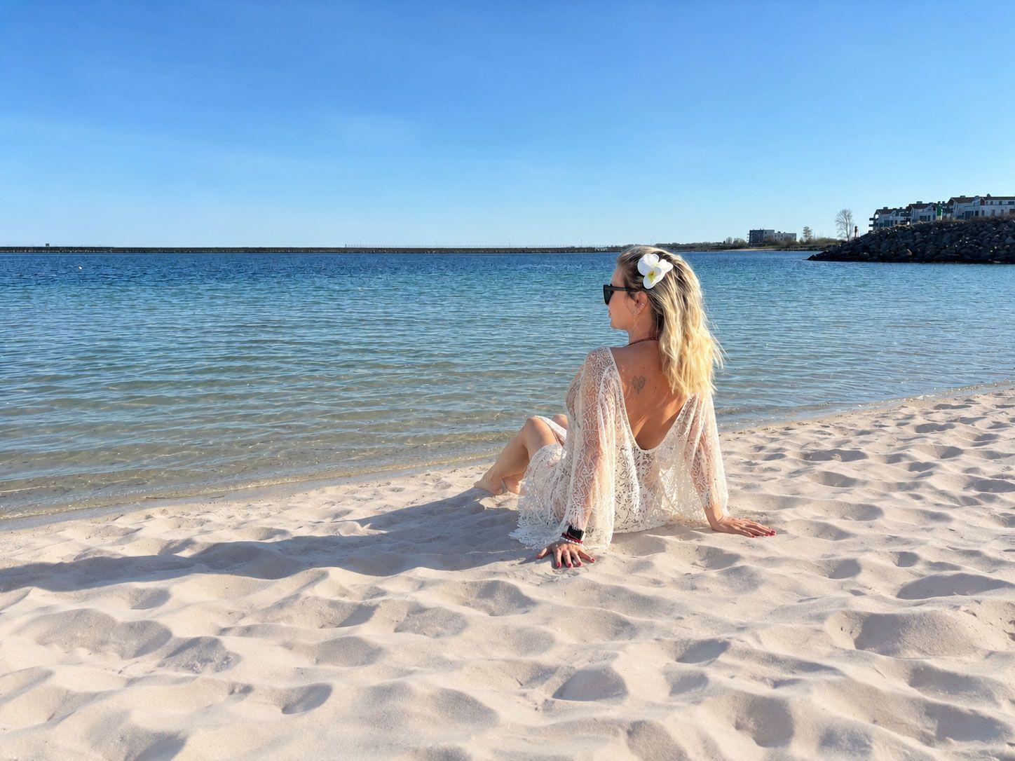 Eine Person sitzt am Strand und blickt auf das Wasser.