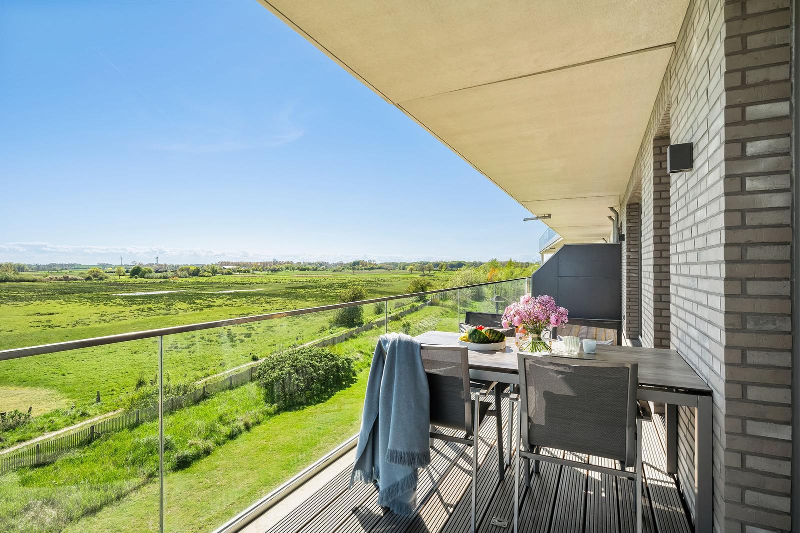 Terrasse mit Tisch, Stühlen und Blick auf grüne Landschaft.