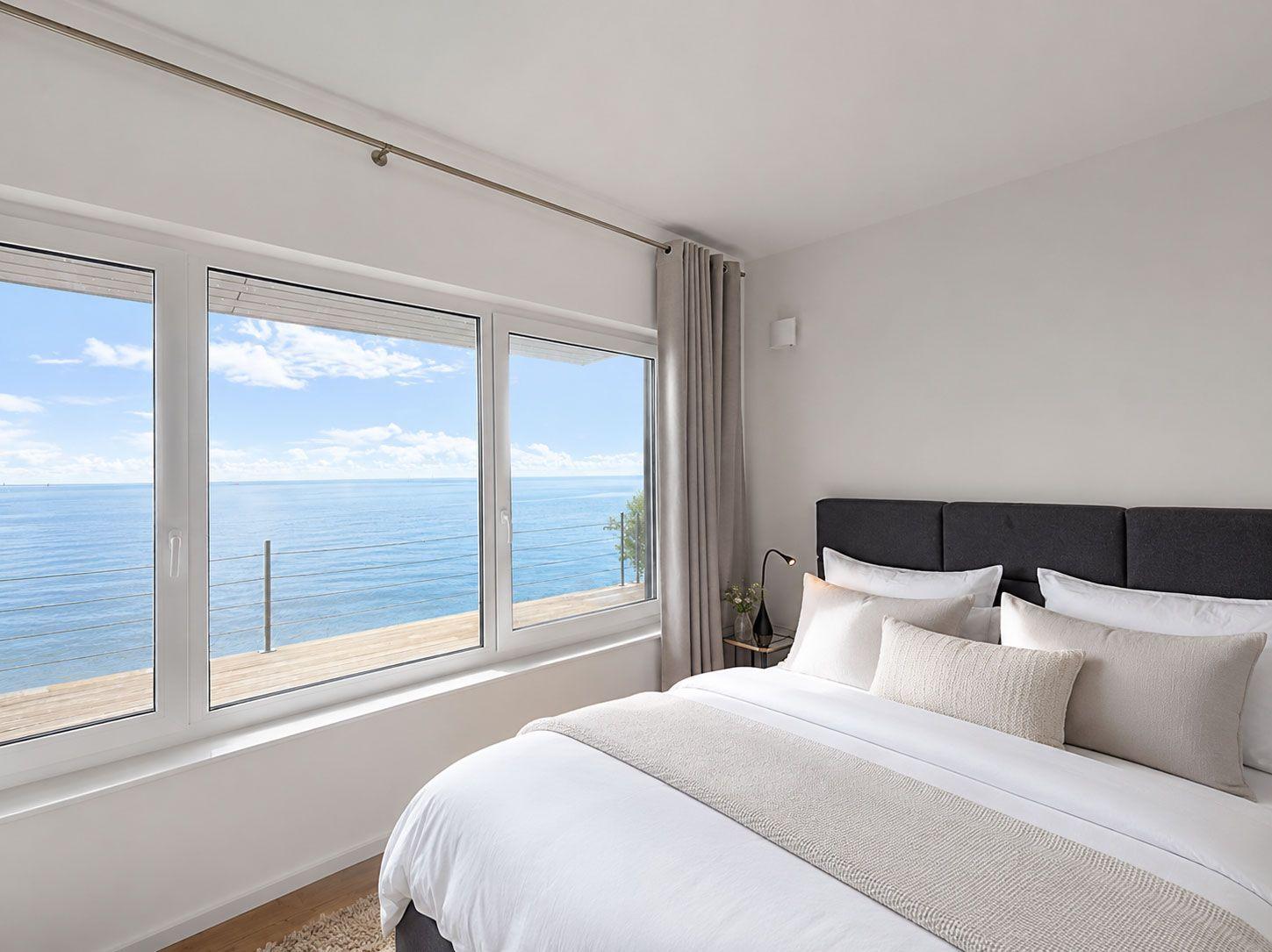 Schlafzimmer mit Blick auf das Meer durch große Fenster.