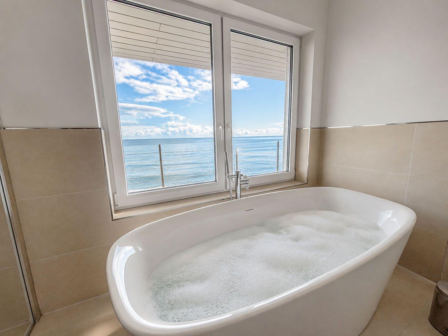 Freistehende Badewanne mit Seeblick durch großes Fenster.
