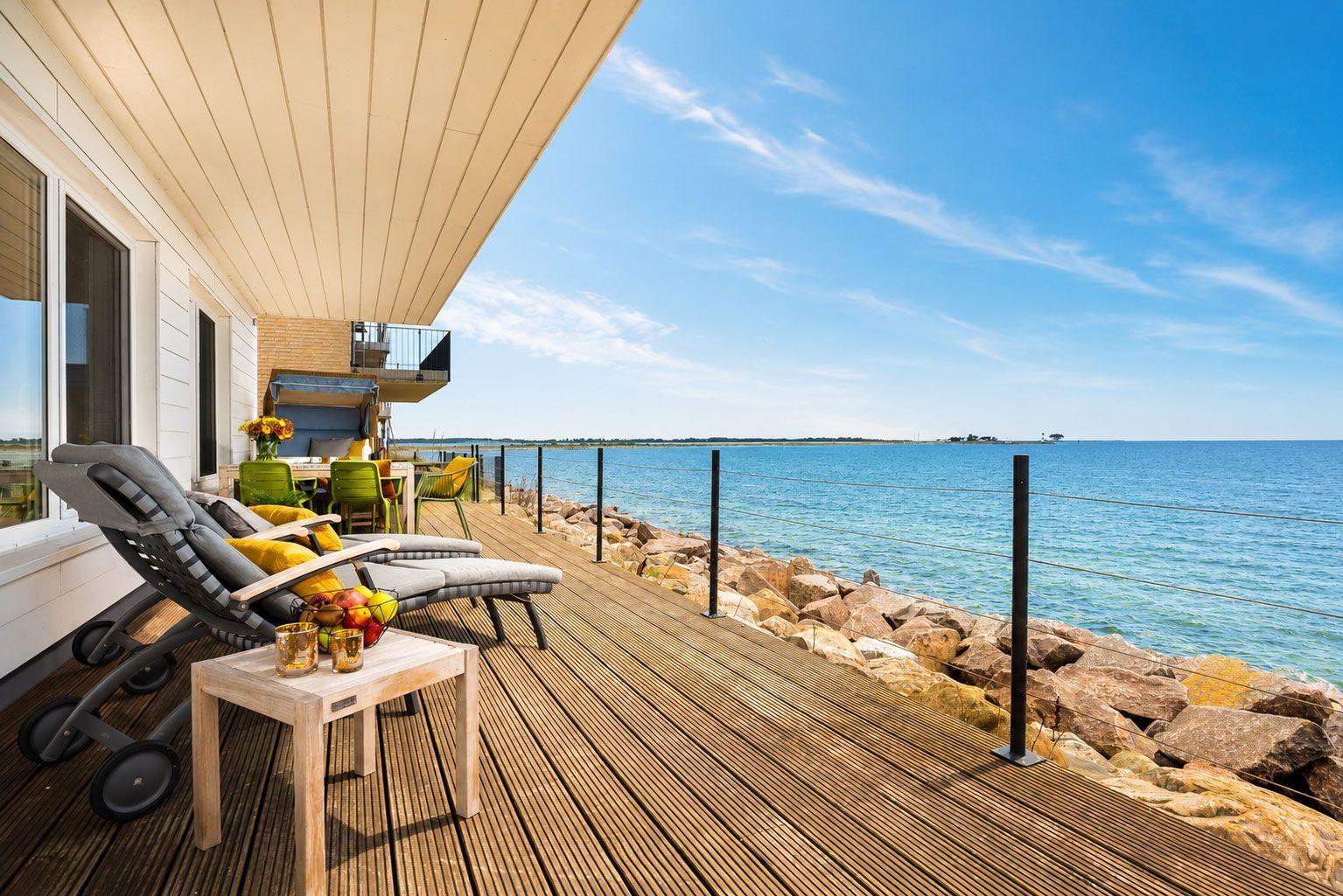 Terrasse mit Liegestühlen und Meerblick. Holzdeck, Steine und klare See.