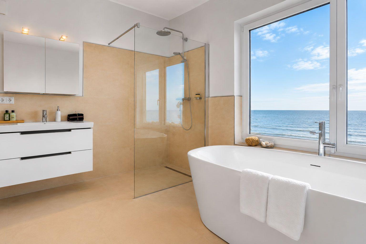 Badezimmer mit freistehender Badewanne und Dusche, Blick auf das Meer durch großes Fenster.