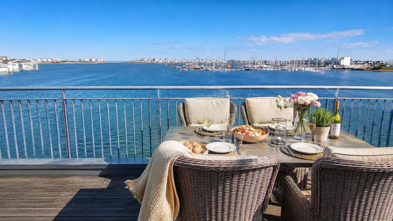 Terrasse mit Tisch und Stühlen für sechs Personen, Blick auf Hafen und Wasser.