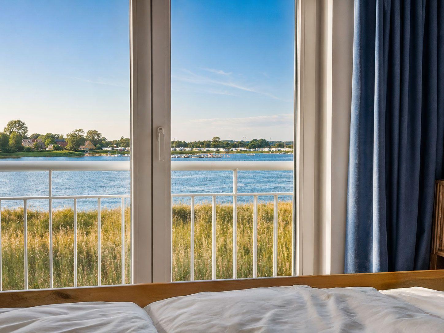 Blick aus dem Schlafzimmer auf einen See mit Ufergras und gegenüberliegenden Häusern.