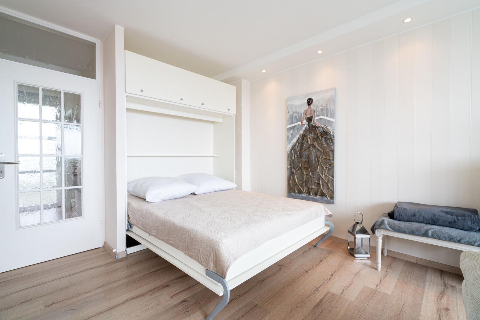 Schlafzimmer mit Klappbett, Wandbild und Holzboden.