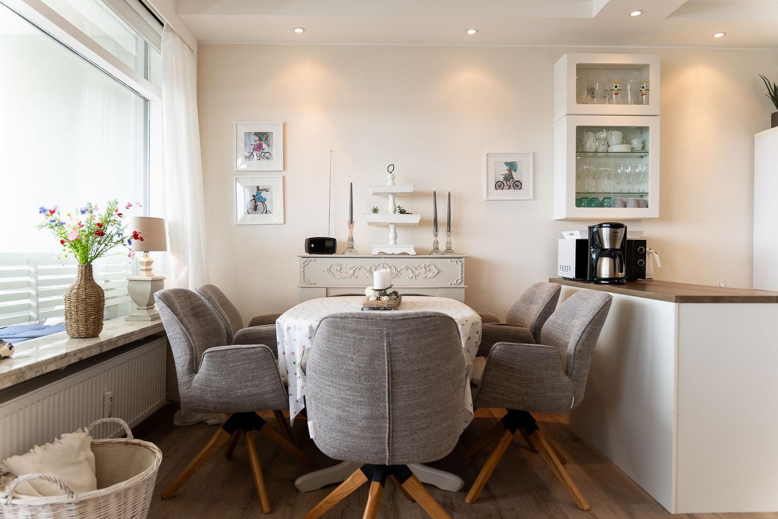 Esszimmer mit runden Tisch, grauen Stühlen und Glasvitrinen an der Wand.