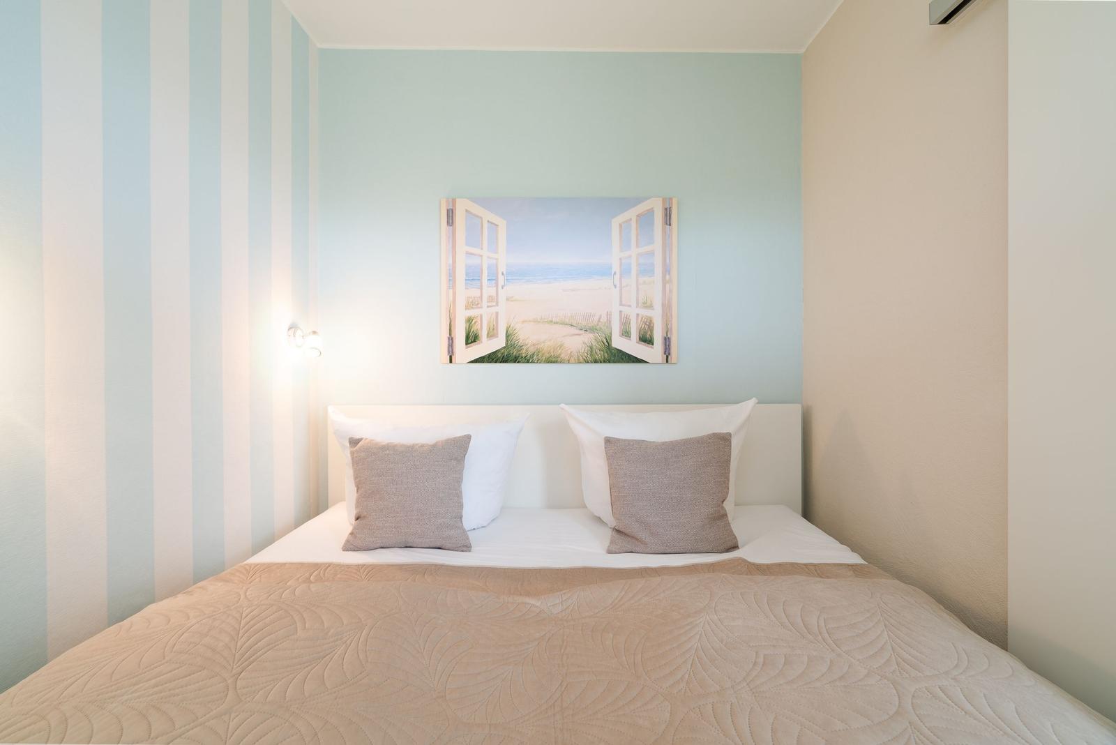 Schlafzimmer mit Bett, Kissen und Wandbild mit Strandmotiv.