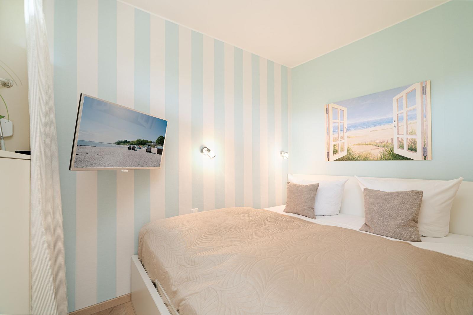 Schlafzimmer mit Bett, Wandbild und TV an der Wand.