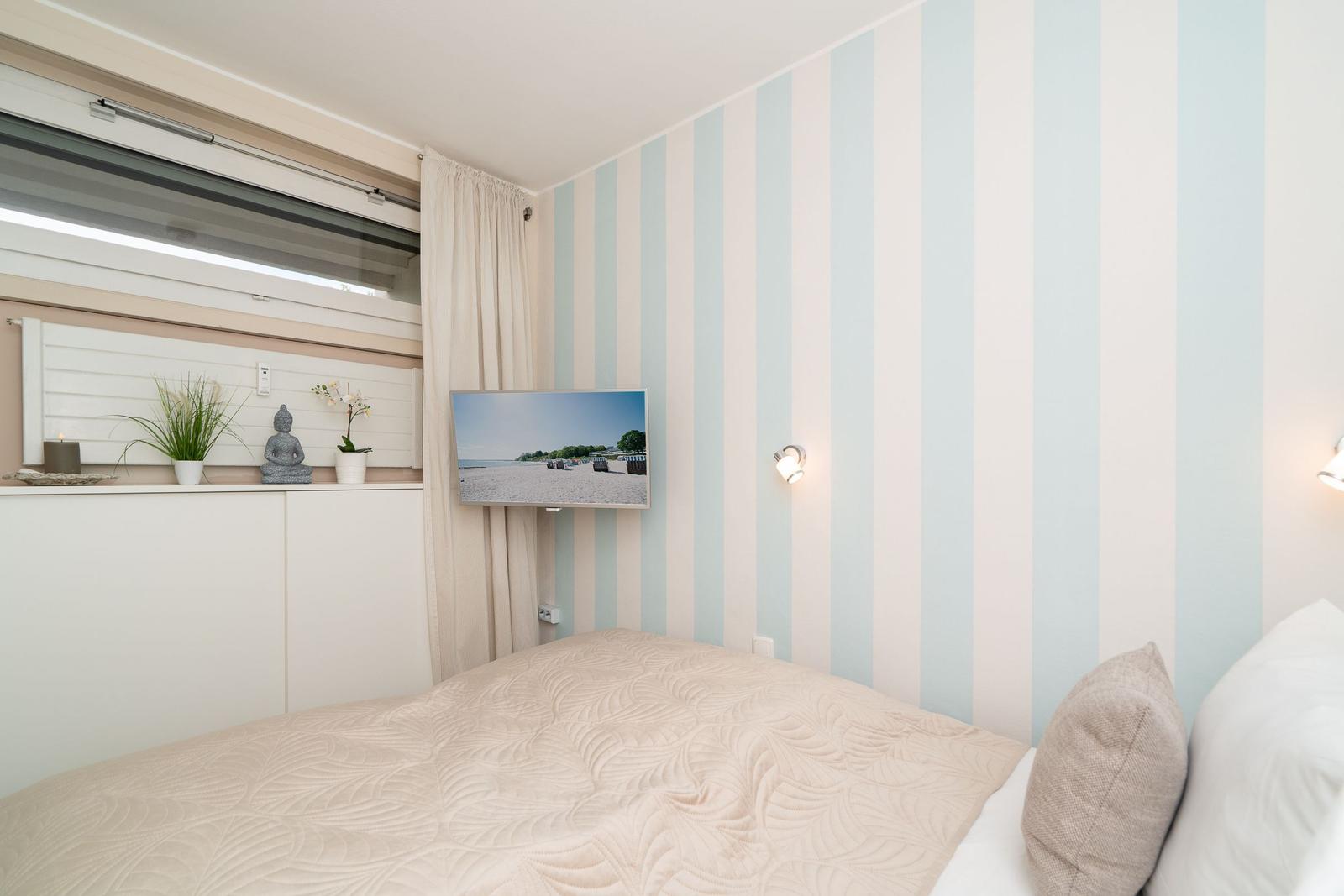 Schlafzimmer mit gestreifter Wand, Bett und TV an der Wand.
