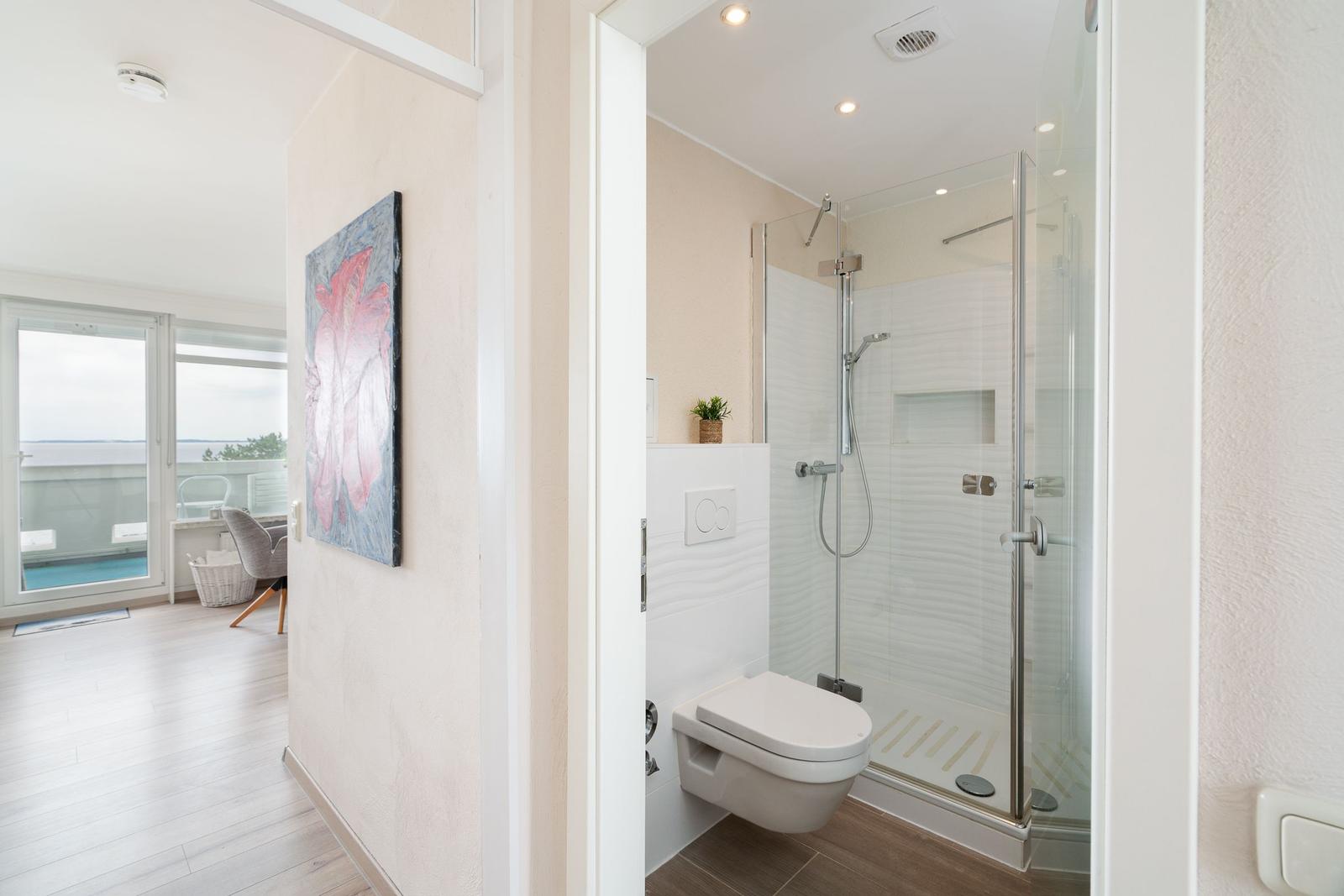 Badezimmer mit Dusche und Toilette. Durchgang zu Wohnbereich mit Balkon.