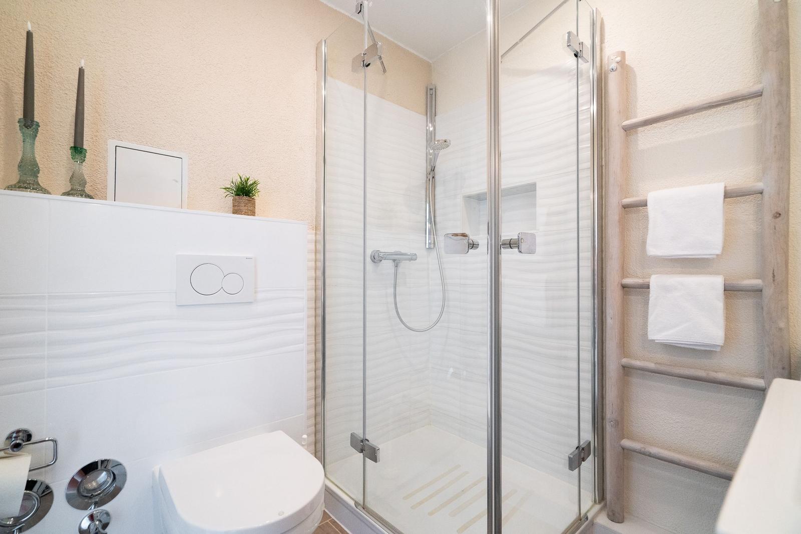 Bad mit Dusche, Toilette und Handtuchhalter an der Wand.