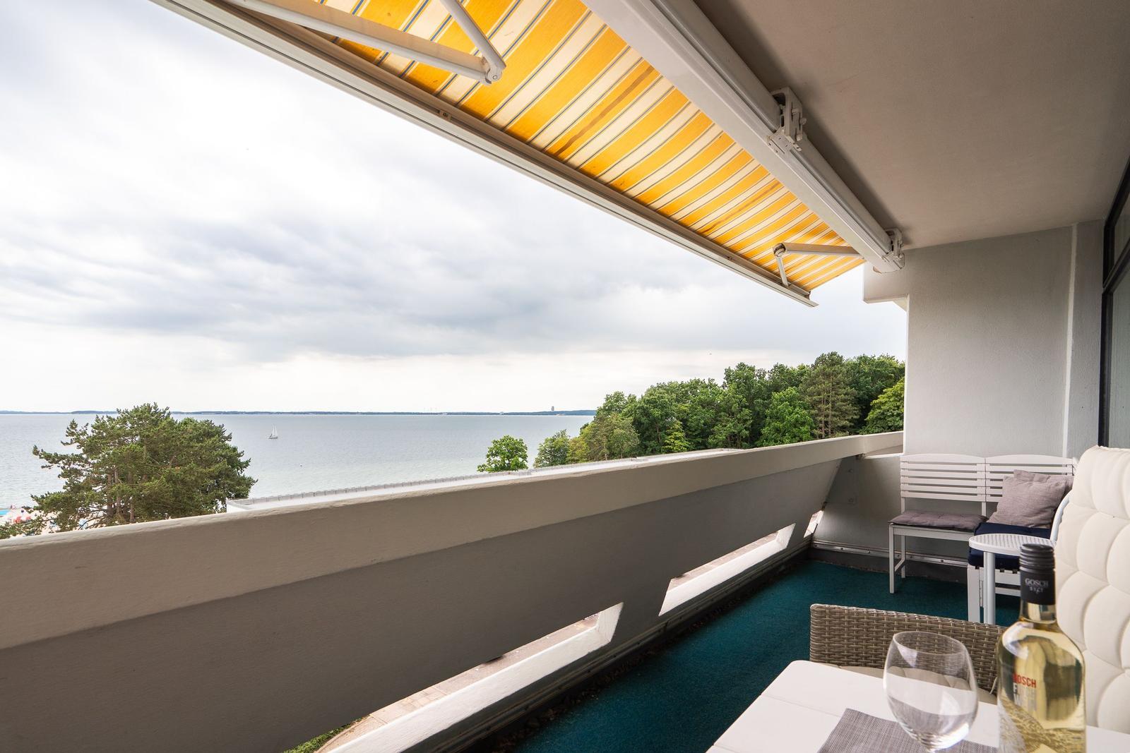 Balkon mit Blick auf See und Wald. Gelber Markise, Tisch und Stühle.