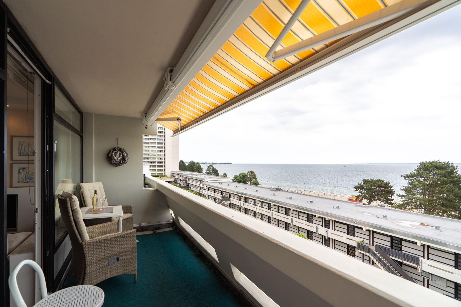 Balcony with yellow awning overlooks sea and buildings.