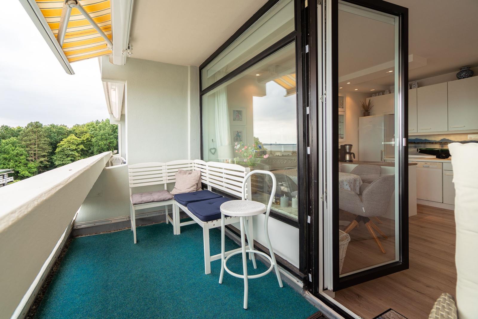 Balkon mit Sitzbank, Tisch und Stuhl. Blick auf Wald. Haustür zur Küche.