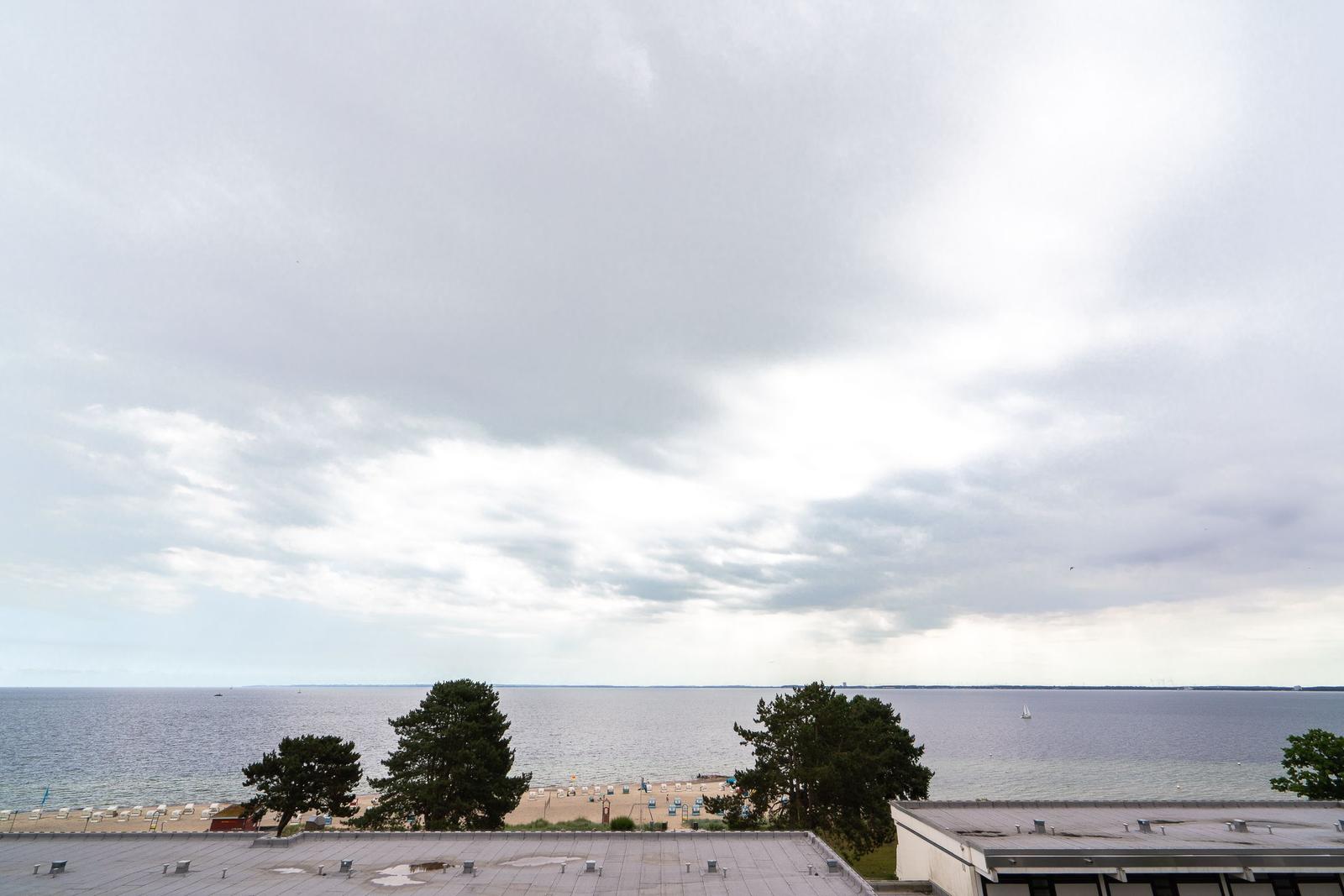 Blick auf Strand und See unter bewölktem Himmel mit Bäumen und Booten