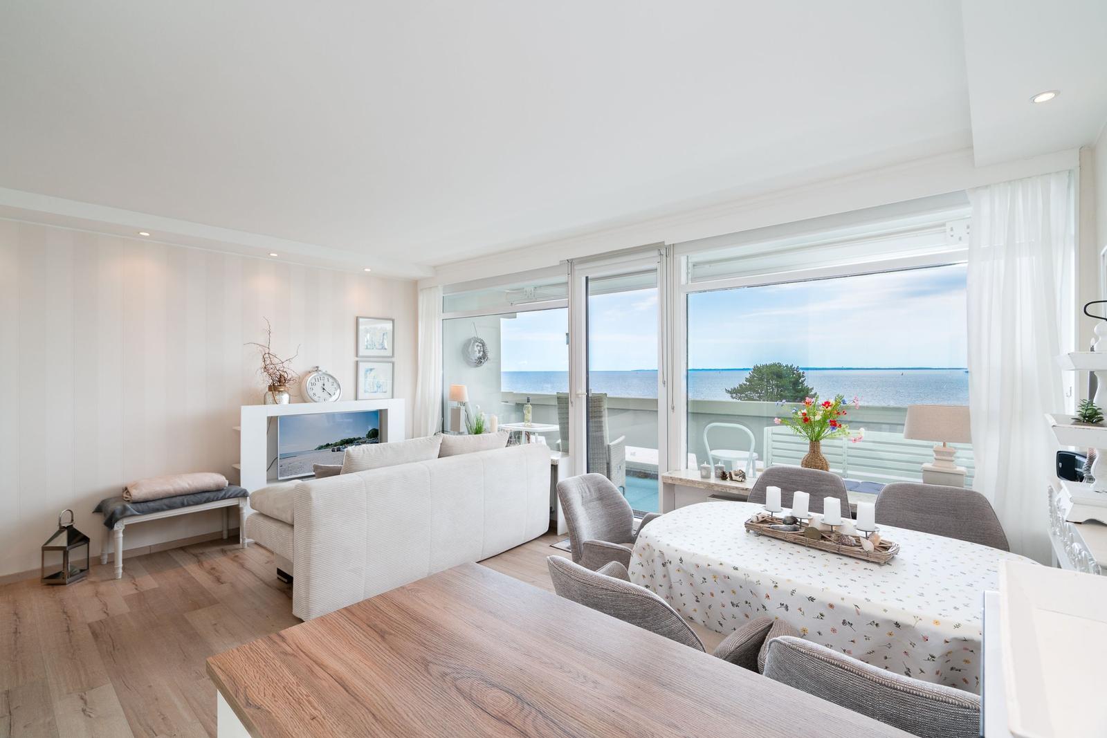 Wohn- und Essbereich mit Meerblick. Holzboden, Sofa, Tisch und Sitzgelegenheiten.
