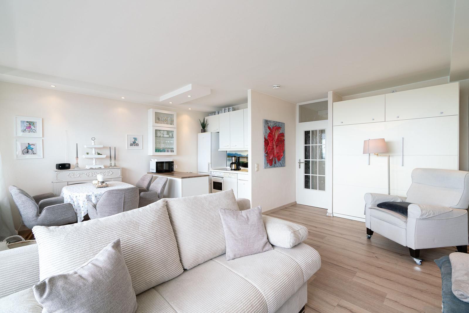 Wohnzimmer mit Sofa, Essbereich und Küche im Hintergrund.