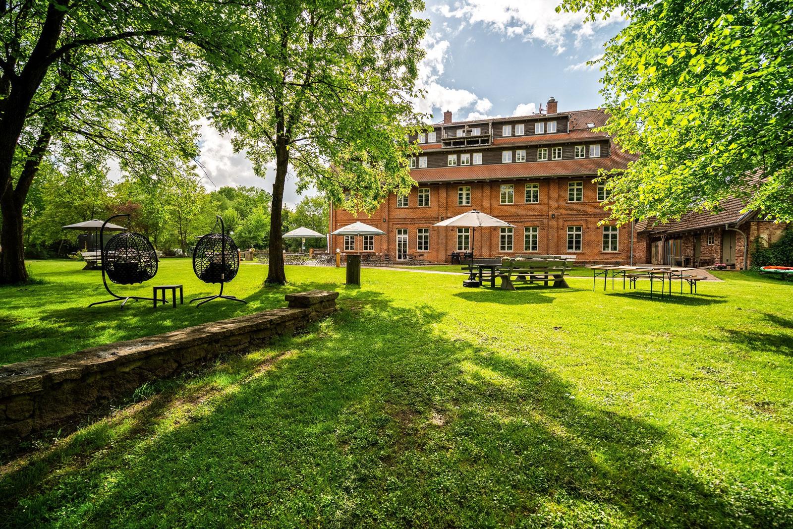 Großer Garten mit Grillplatz, Tischen und Hängesesseln vor einem Backsteinhaus.