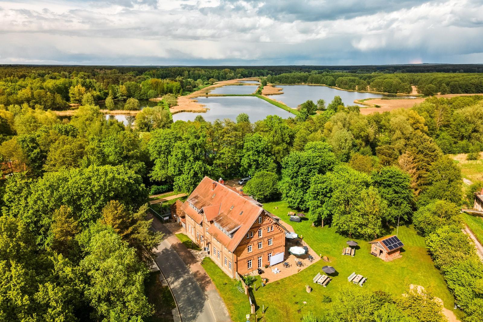 Rotes Backsteingebäude mit Terrasse, umgeben von Wald und Teichen.
