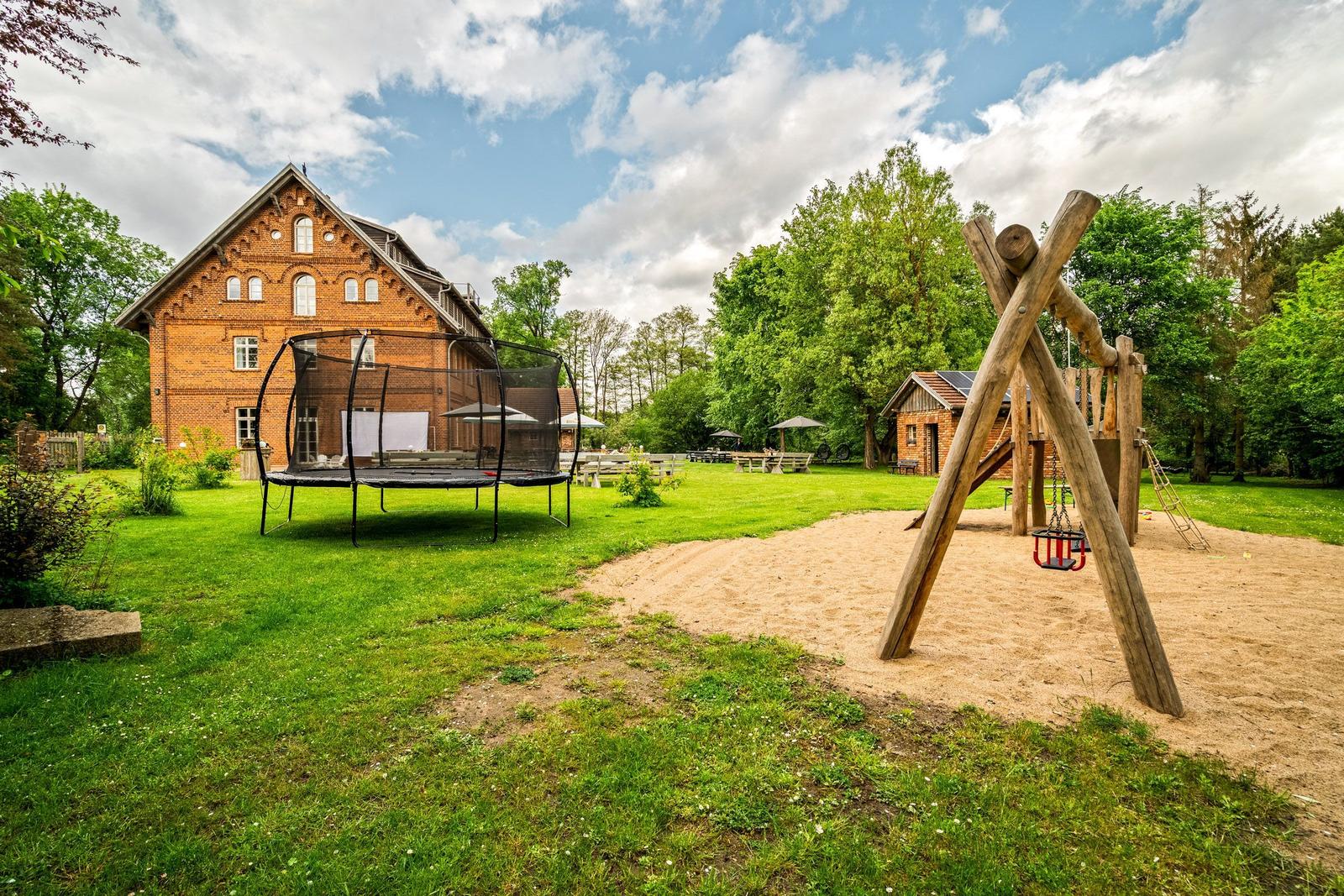 Haus mit Spielplatz, Trampolin und Sandkasten auf grünem Grund.