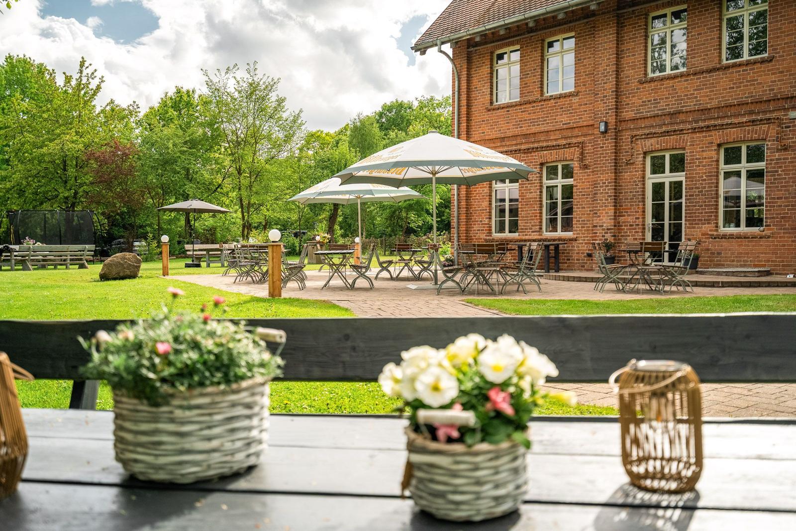 Roter Backsteinbau mit Terrasse, Tischen, Stühlen und Sonnenschirmen im Garten.