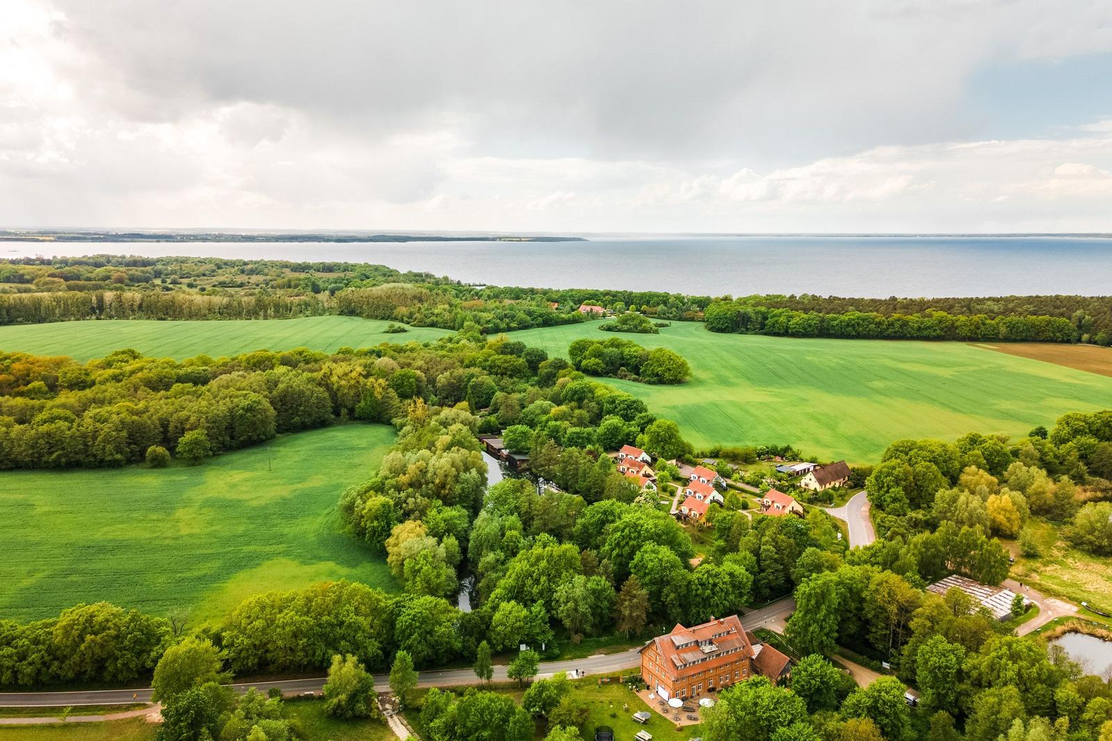 Ländliche Umgebung mit Wald, Feldern und einem See im Hintergrund.