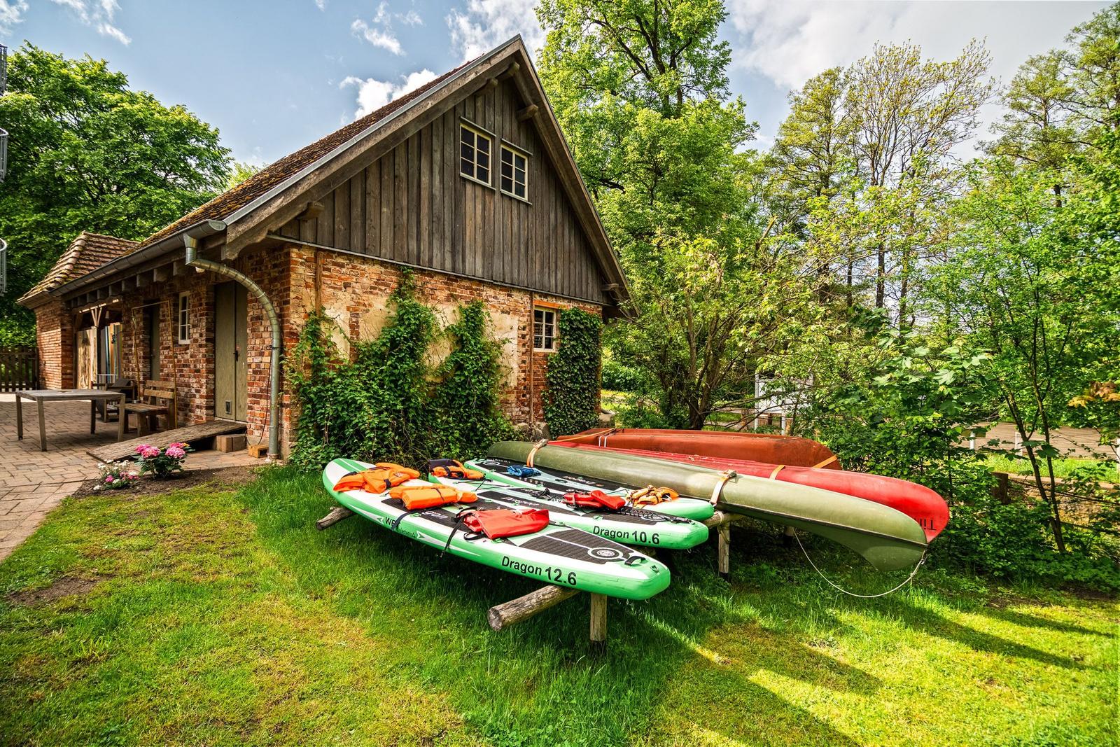 Holzhaus mit Kanu und Stand-Up-Paddleboards im Grünen.