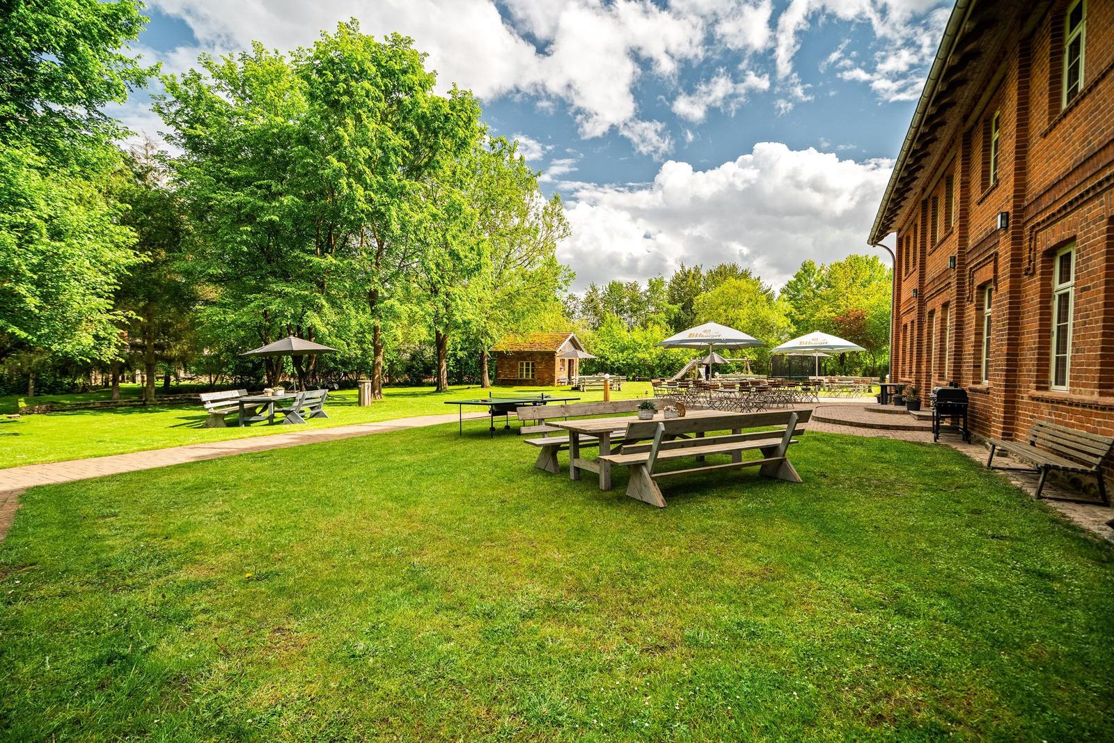Großer Garten mit Tischen, Bänken und Grillplatz neben Backsteinhaus.