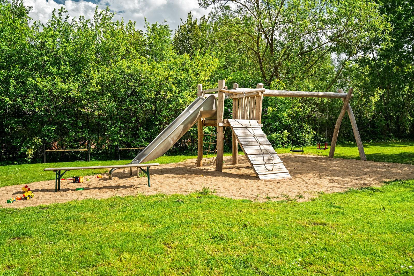Hinterhof mit Spielplatz, Rutsche, Schaukel und Sandkasten. Grasfläche und Bäume im Hintergrund.