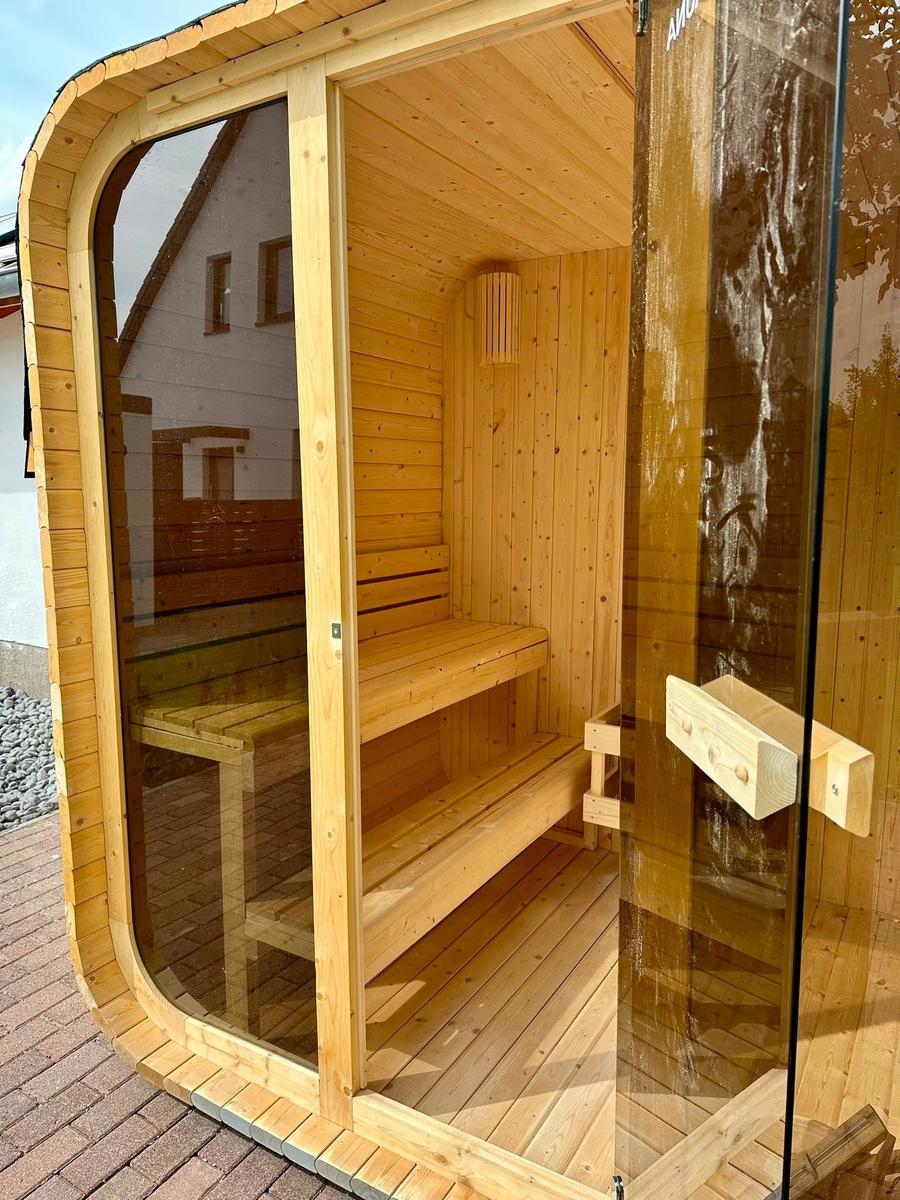 Außenliegende Holzsauna mit Glasfront und mehreren Sitzstufen.