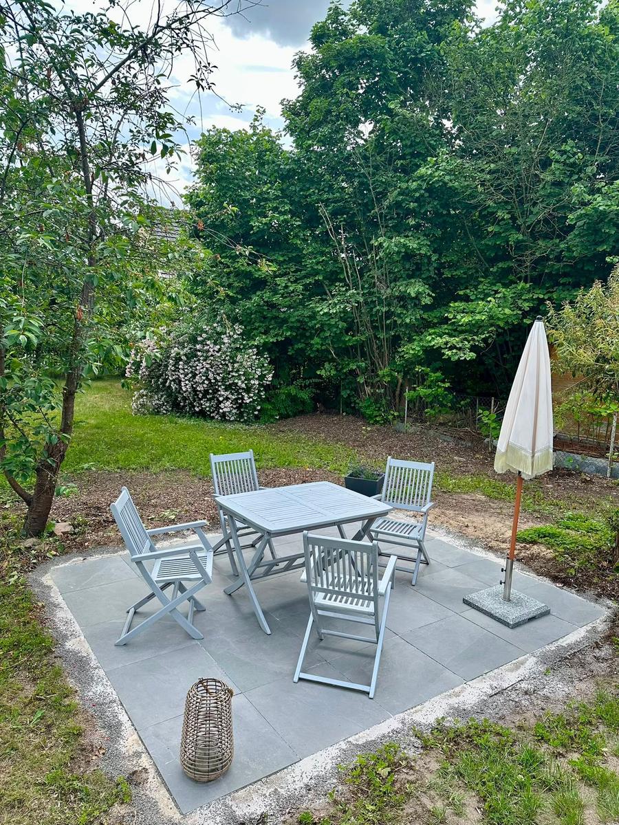Hinterhof mit Tisch, vier Stühlen und geschlossenem Sonnenschirm auf Steinplatten.