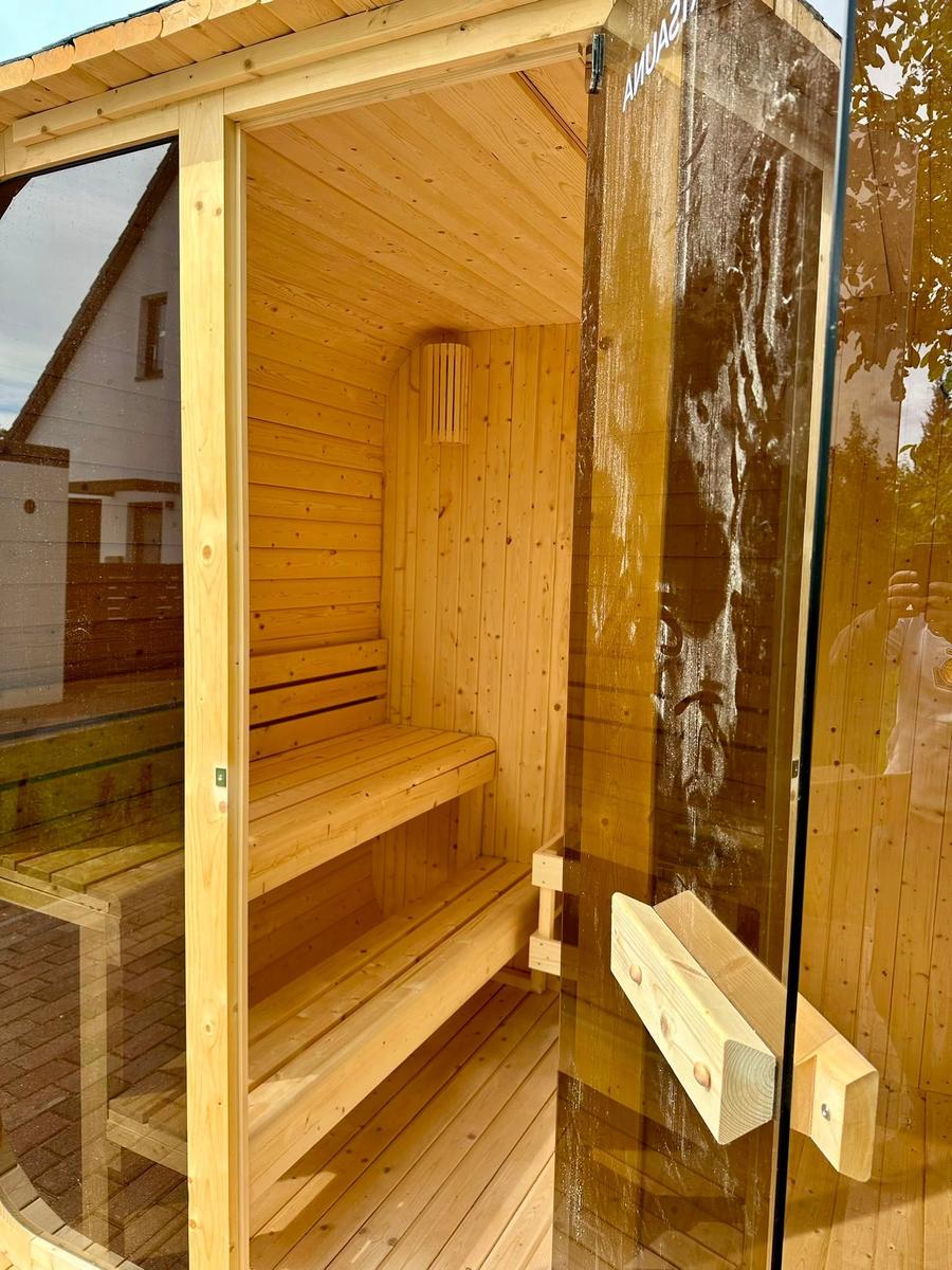 Holzsauna mit Sitzbänken und Glasfront. Tür mit Holzgriff und Aufschrift.