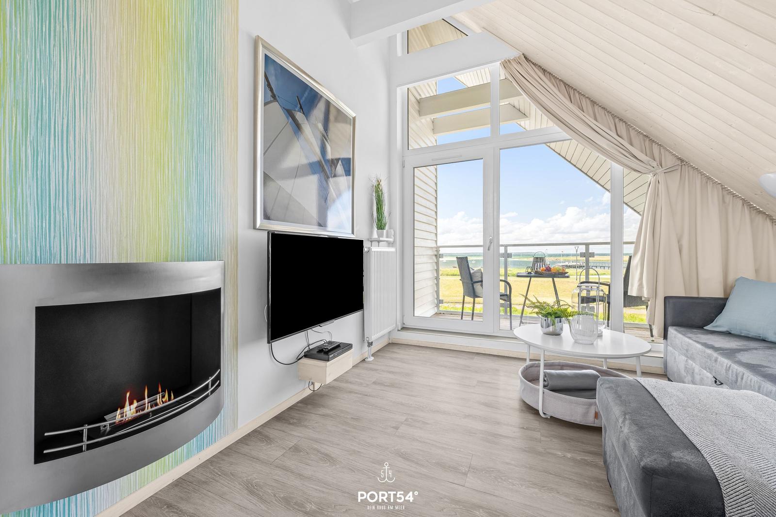 Wohnbereich mit Kamin, Fernseher und Blick auf Balkon mit Meerblick.