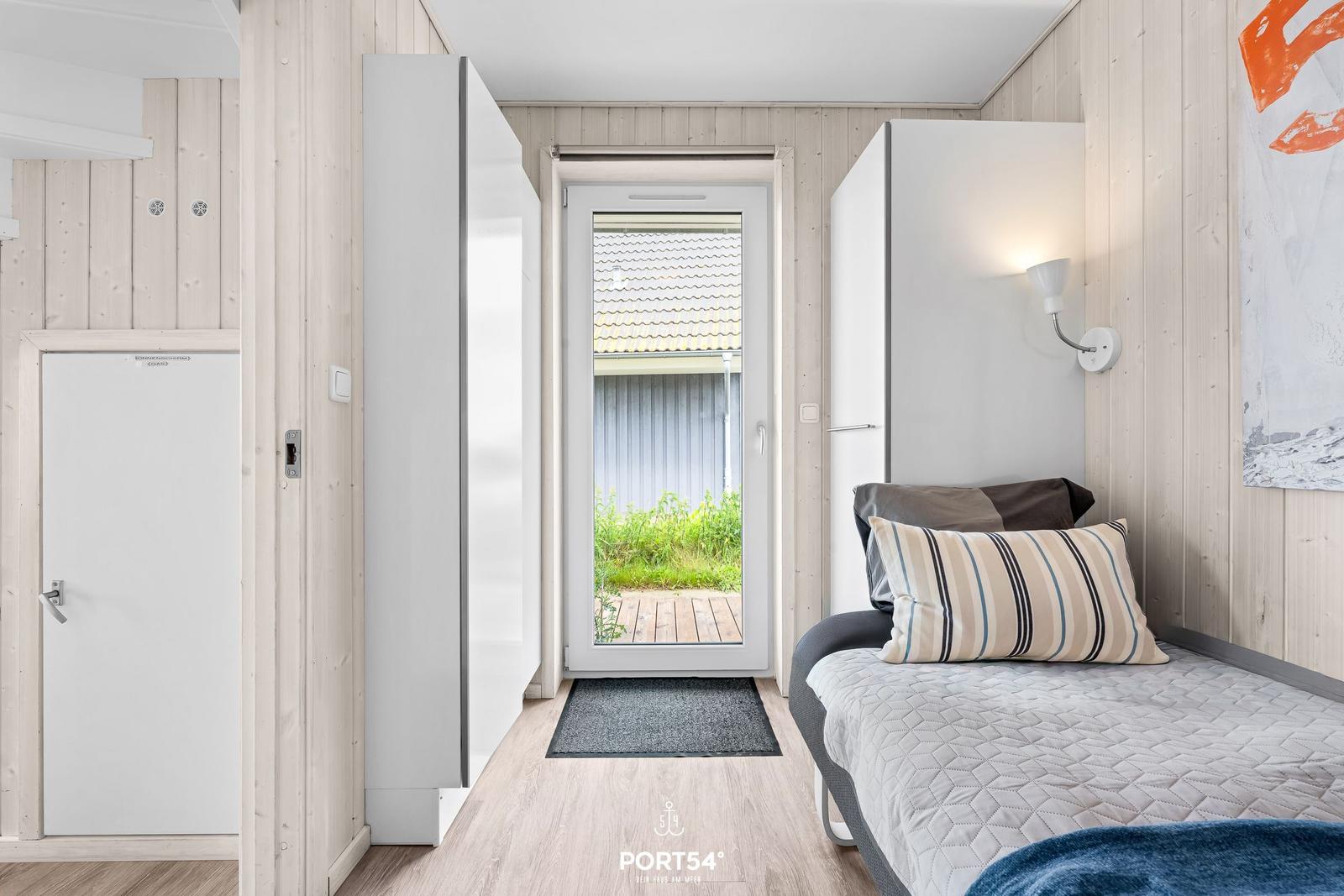 Schlafzimmer mit Bett, Tür zum Balkon und weißen Schränken an den Wänden.