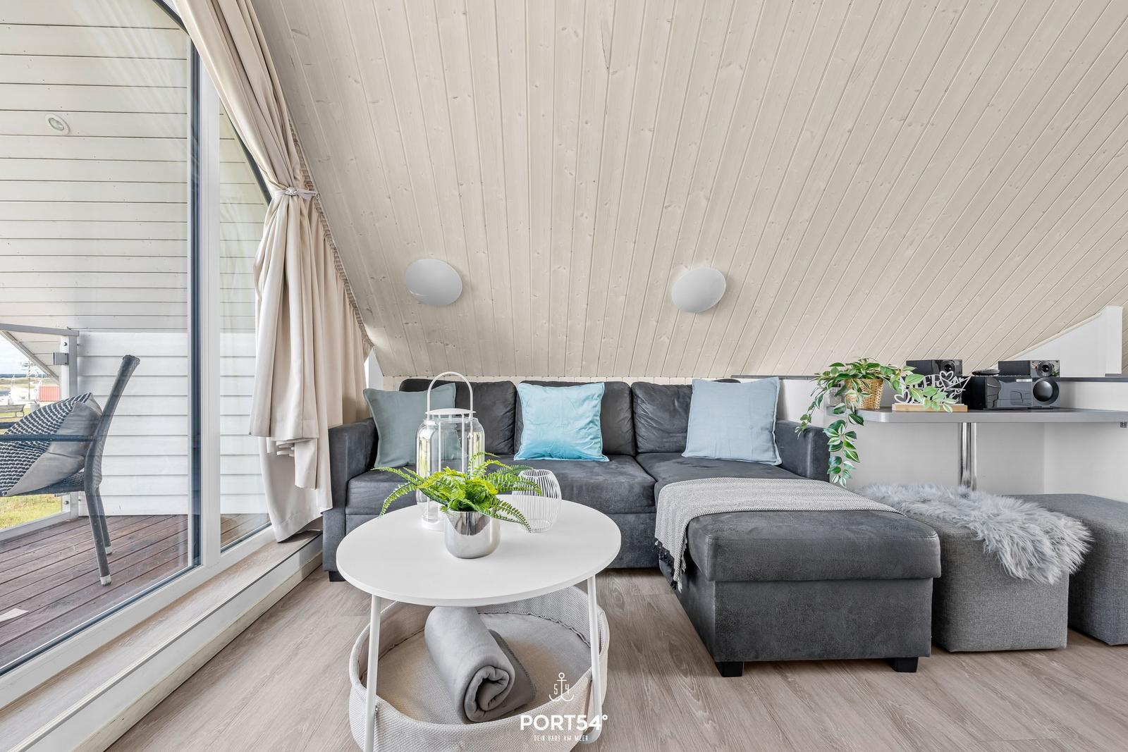 Wohnbereich mit grauem Sofa, runder Tisch und Blick auf Balkon.