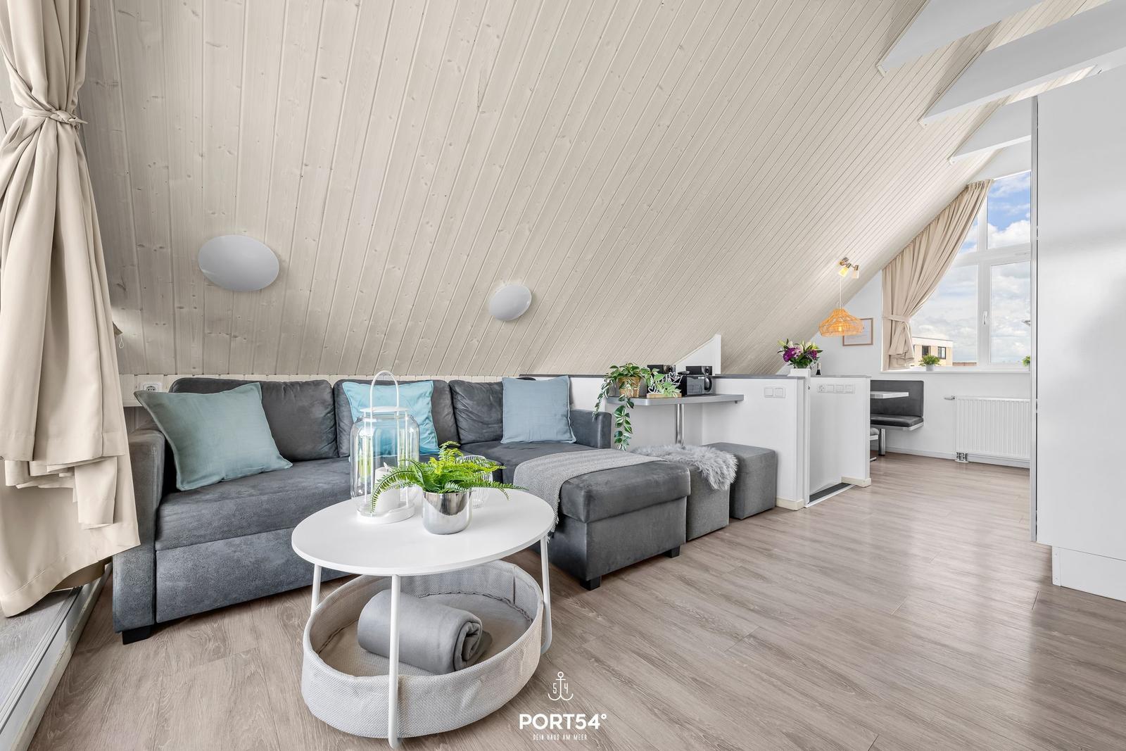 Wohnbereich mit grauem Sofa, runder Tisch und Holzboden unter schrägem Dach