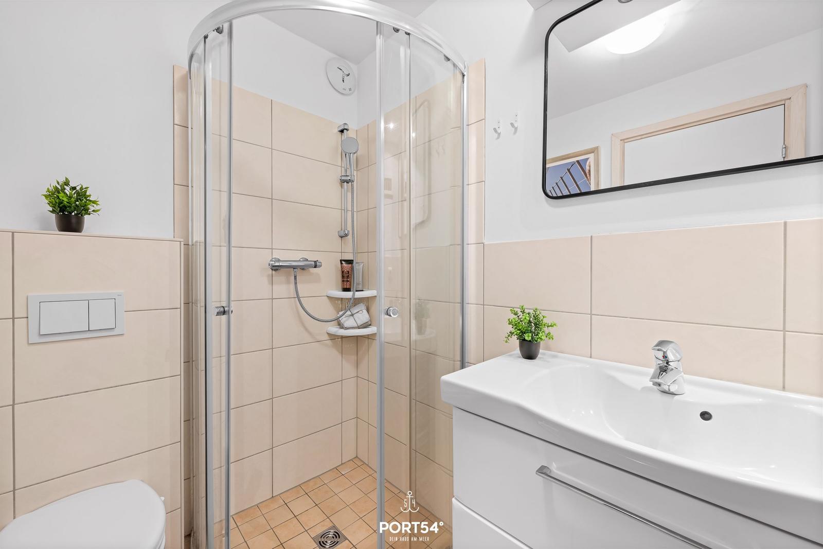 Badezimmer mit Dusche, Waschbecken und Toilette. Fliesenwand und Spiegel.