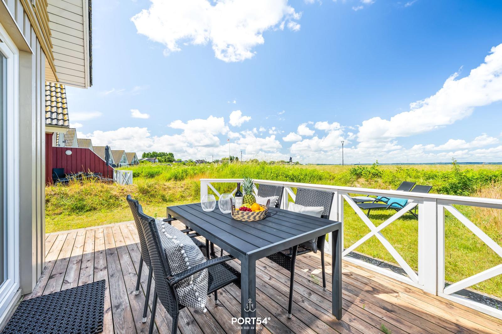 Terrasse mit Tisch und Stühlen, Blick auf Grasland und Himmel.