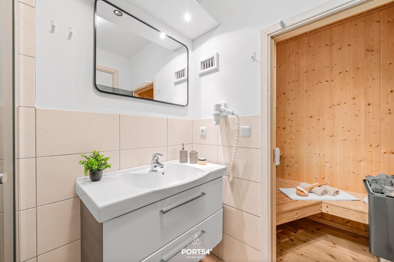 Bad mit Waschbecken, Spiegel und Sauna im Hintergrund.