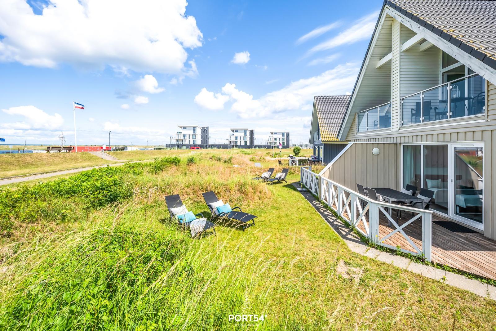 Haus mit Terrasse und Liegestühlen auf grünem Grundstück